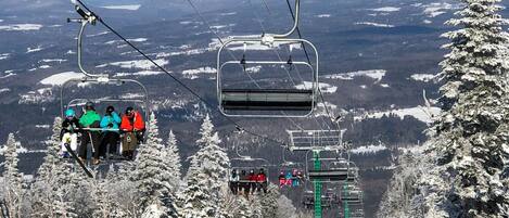 A ski lift with passengers, surrounded by snow-covered trees and a mountainous landscape.