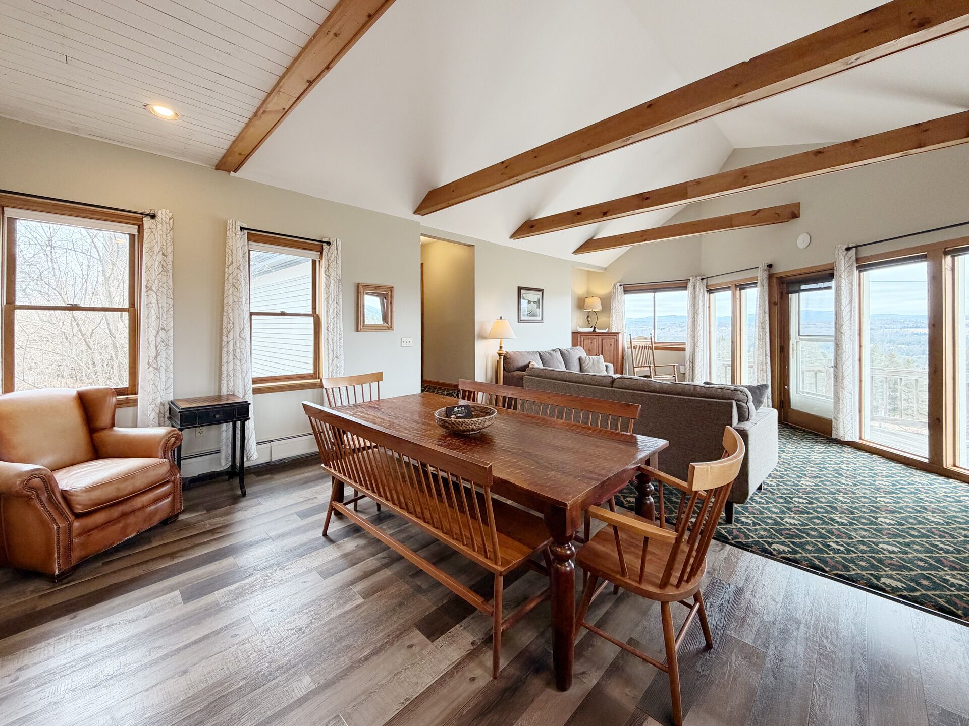 A spacious room with a wooden dining table, leather sofa, and large windows offering a view.