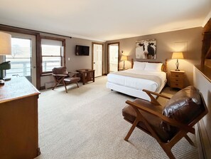 A hotel room with a large bed, a desk, a chair, a television, and a door leading to a balcony. - The Wildflower Inn (Lyndonville)