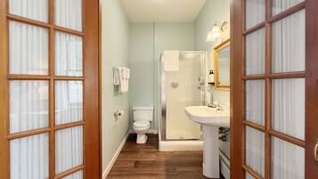 A bathroom with a toilet, shower, and sink, wooden flooring, and frosted glass doors.