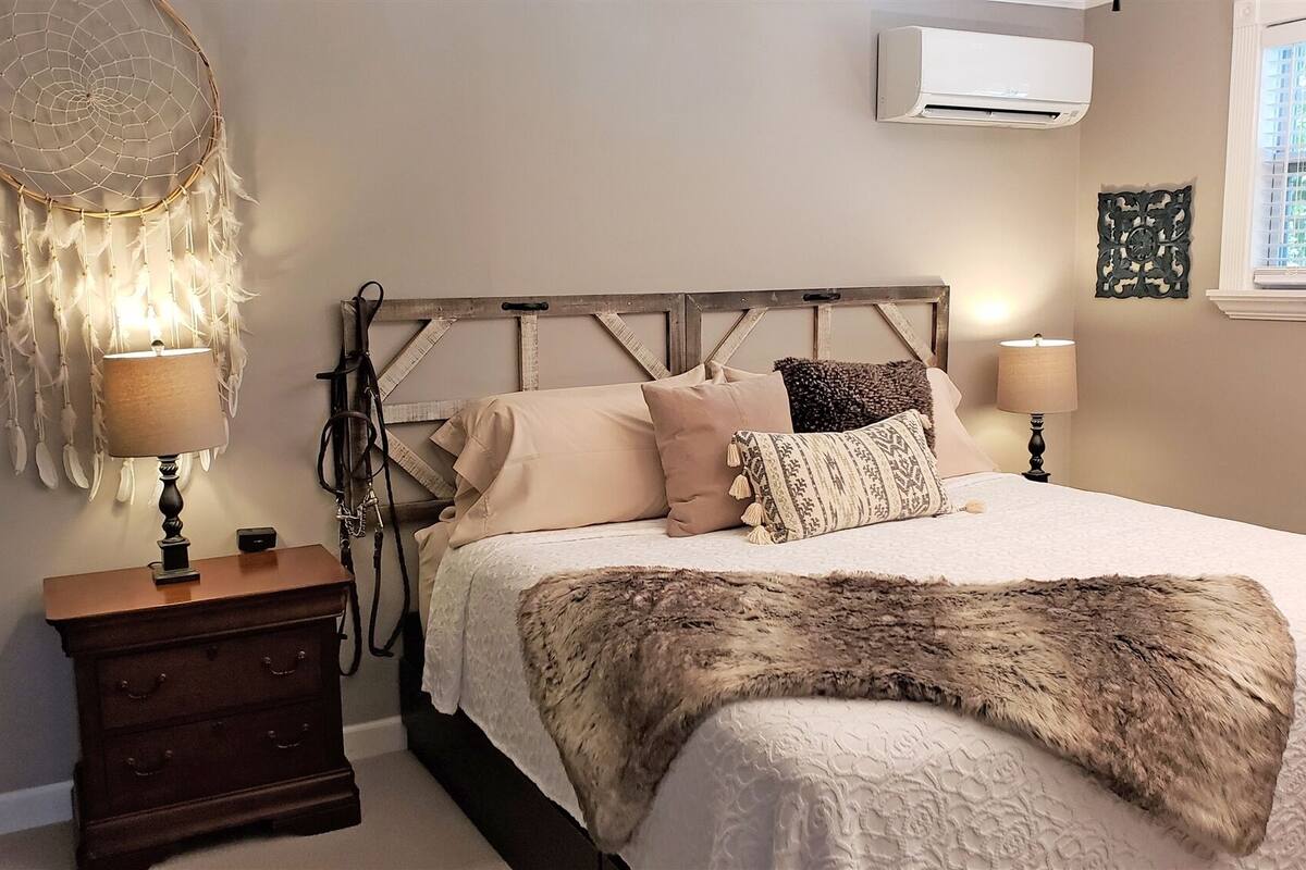 A bedroom with a bed, nightstands, a dreamcatcher, and an air conditioner.