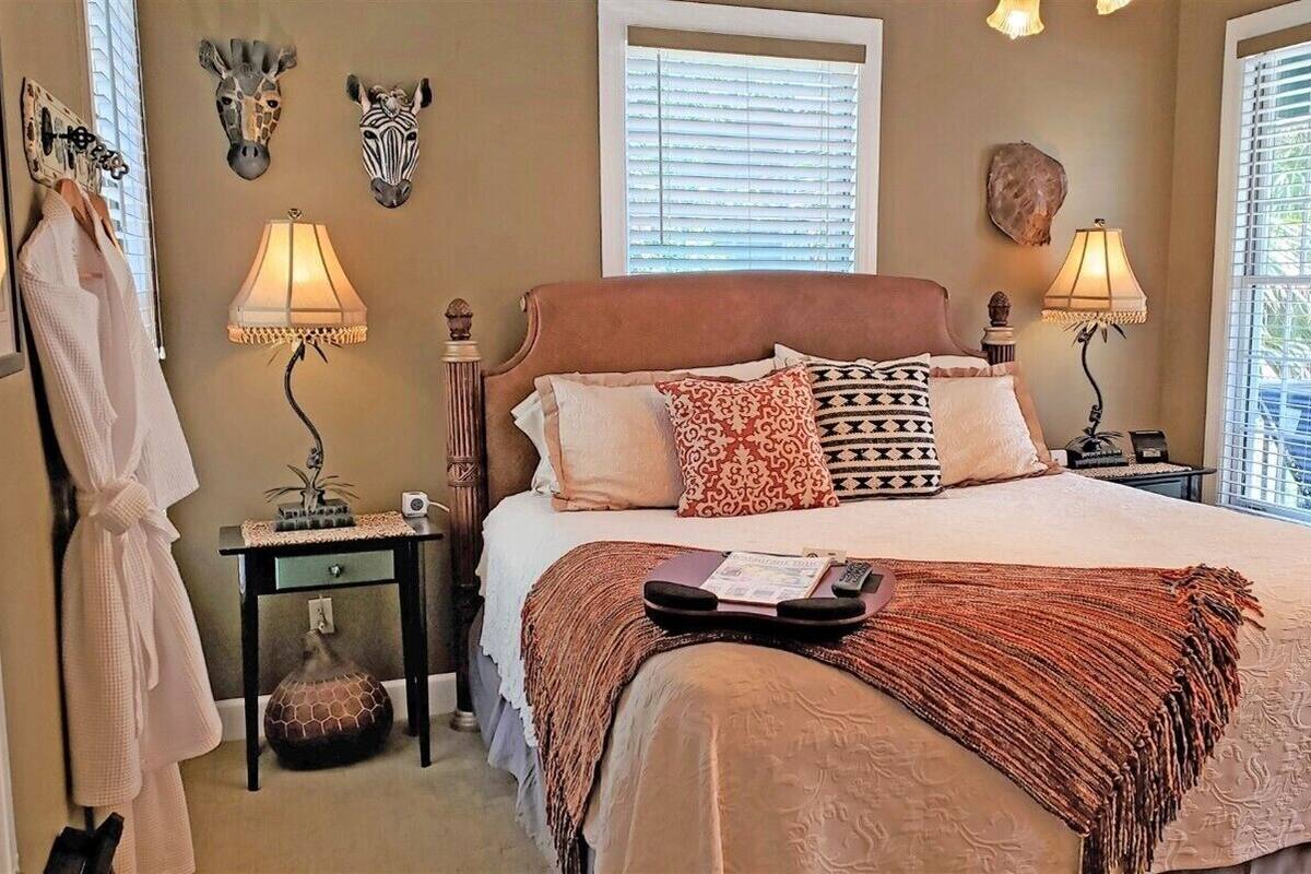 A bedroom with a large bed, two bedside lamps, a nightstand, a robe hanging on a hook, and decorative wall art.