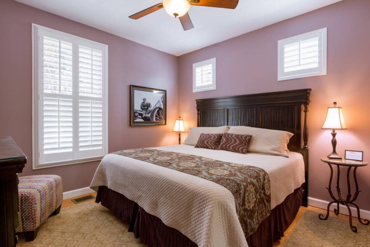 A bedroom with a large bed, two bedside lamps, a ceiling fan, and a framed picture on the wall.
