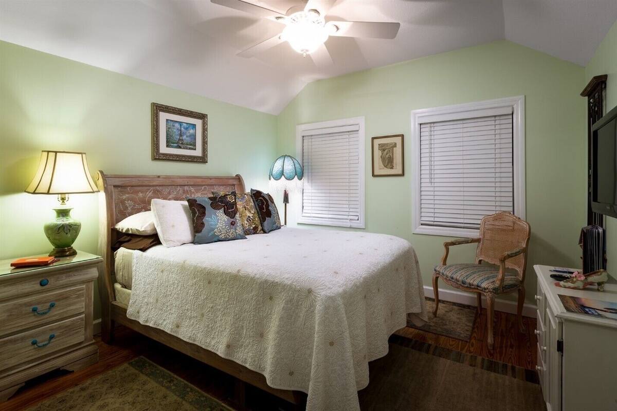 A bedroom with a bed, nightstand, lamp, chair, and a ceiling fan.