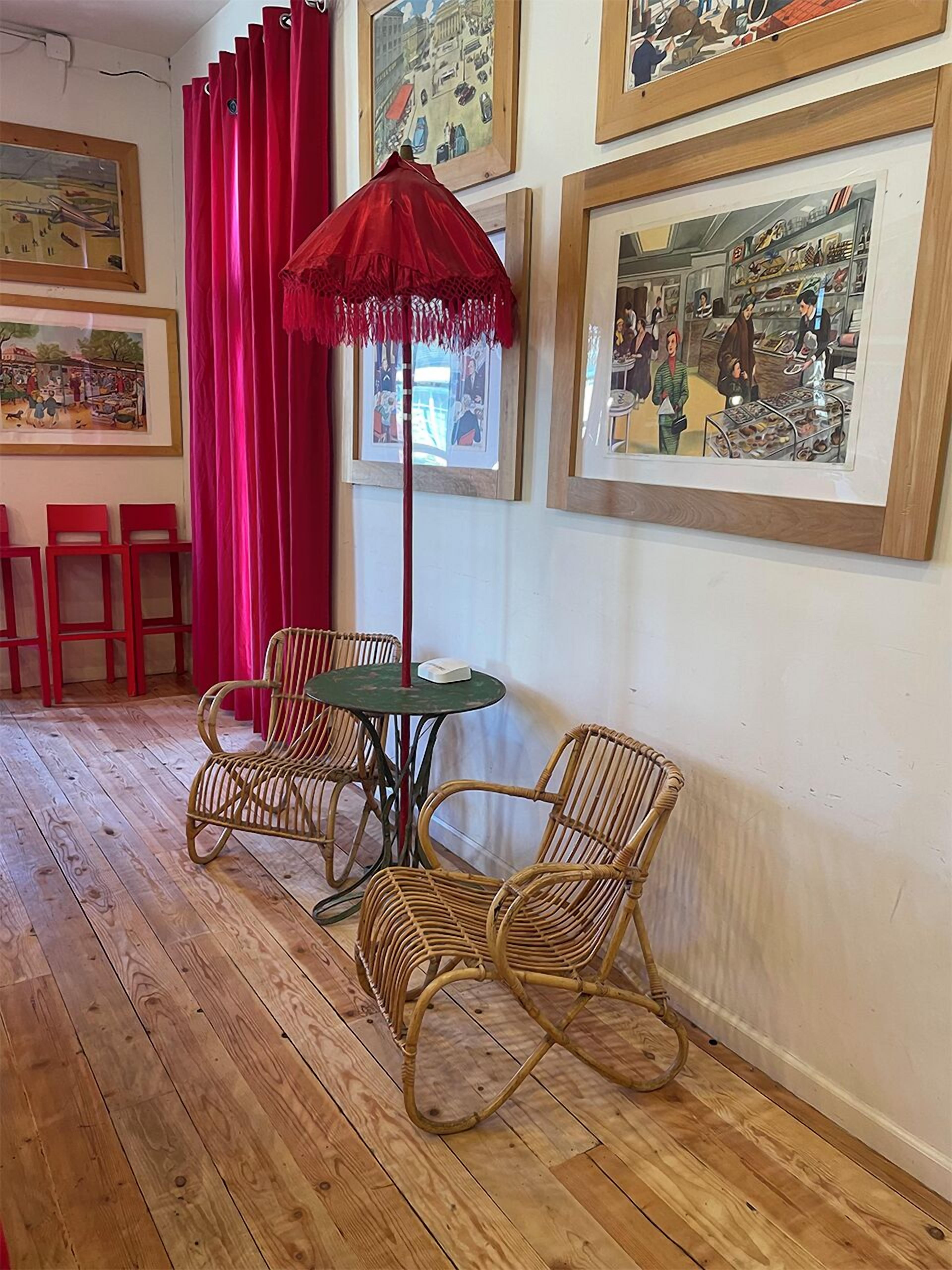Une pièce avec un plancher en bois, des chaises en osier, une petite table ronde et un parapluie rouge.