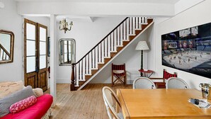 A living room with a wooden staircase, a dining area with a wooden table and chairs, a red sofa, and a large sports-themed wall mural. - Metro Hotel and Cafe (Petaluma)