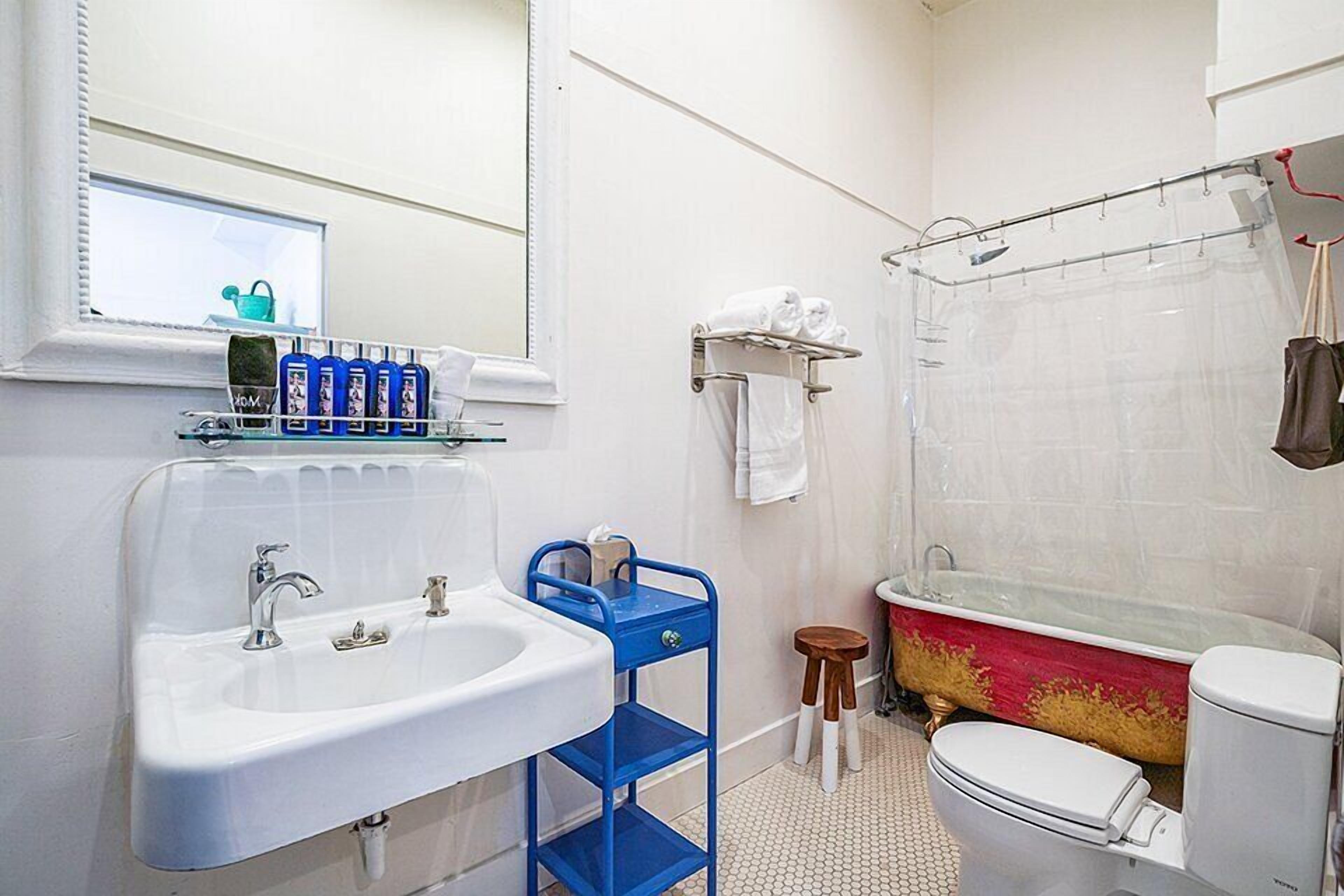 Une salle de bain avec un lavabo blanc, un porte-serviettes bleu et une baignoire rouge.