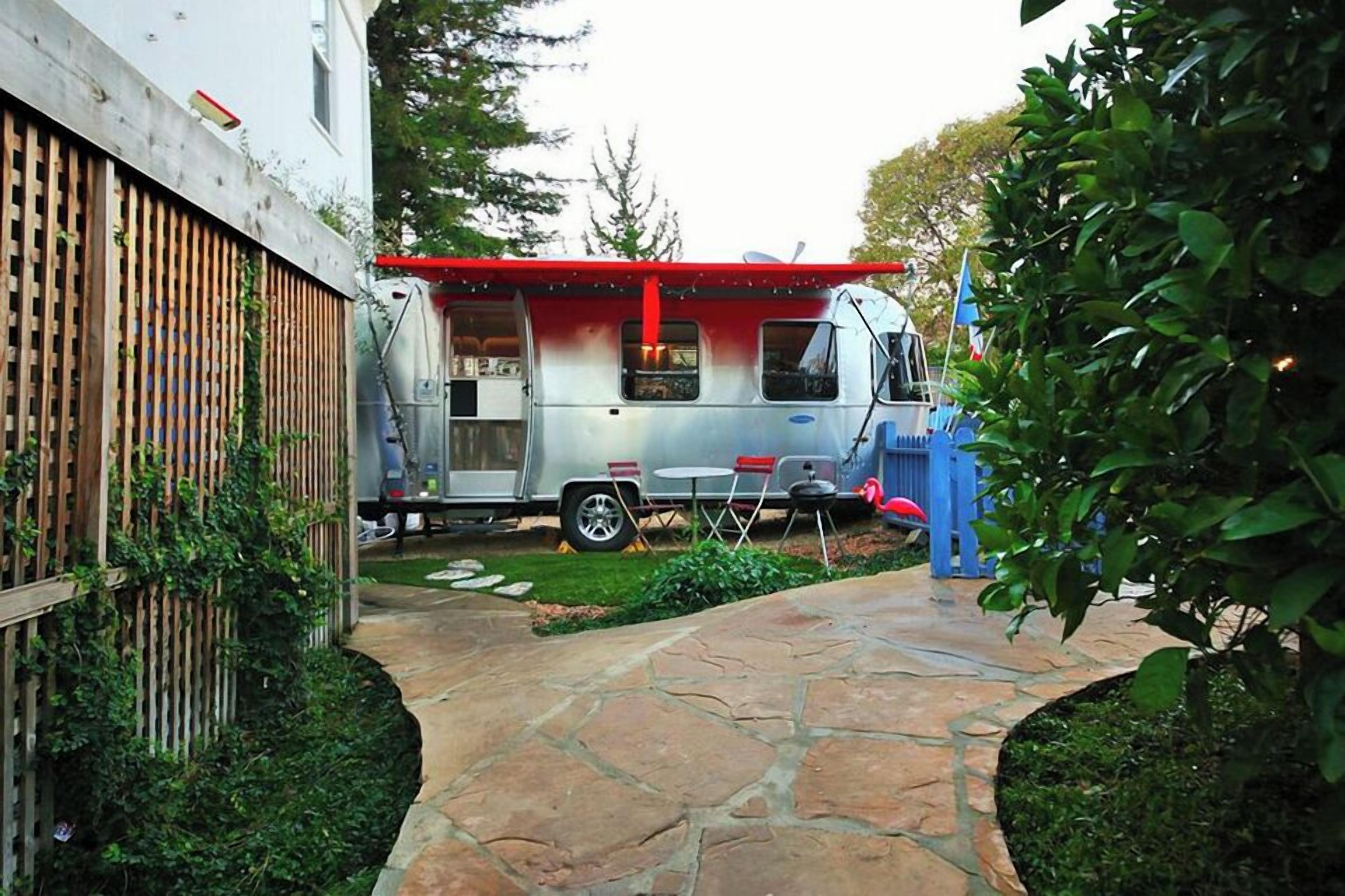 A food truck parked in a backyard with a stone pathway, a wooden fence, and a small table and chairs.