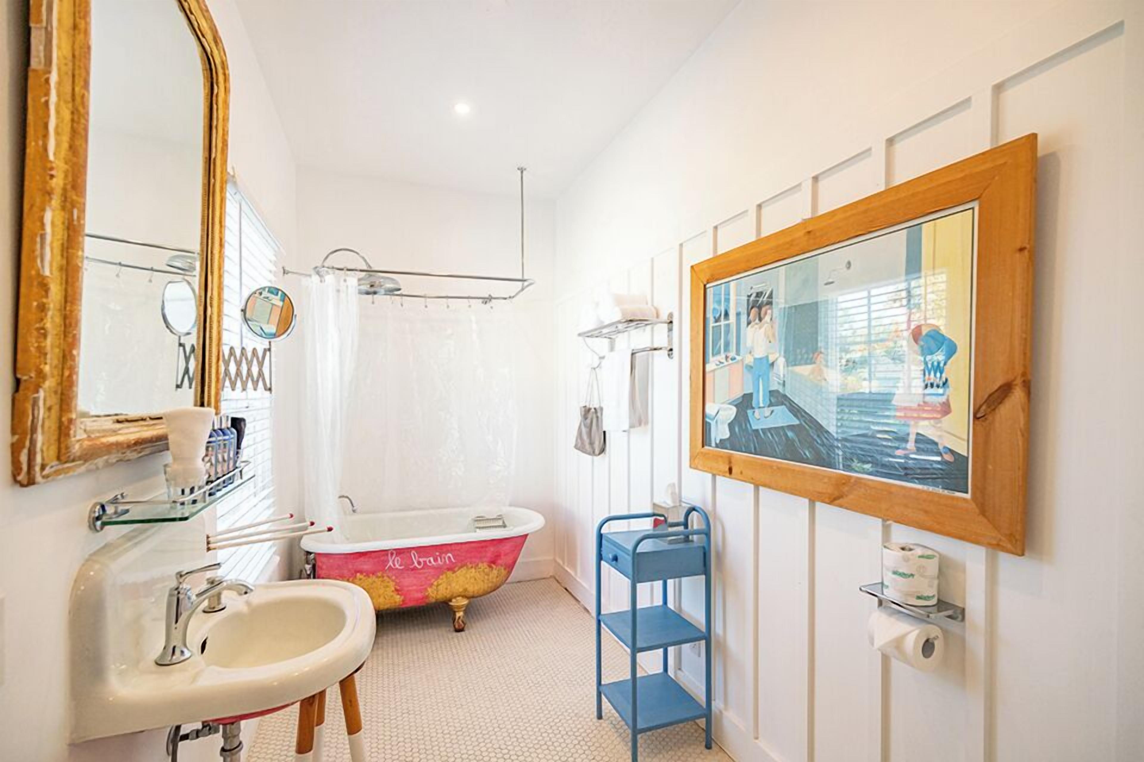 A bathroom with a white sink, a pink bathtub, a blue shelf, and a large mirror.
