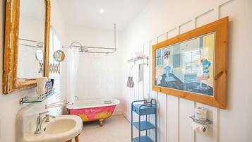 A bathroom with a white sink, a pink bathtub, a blue shelf, and a large mirror.