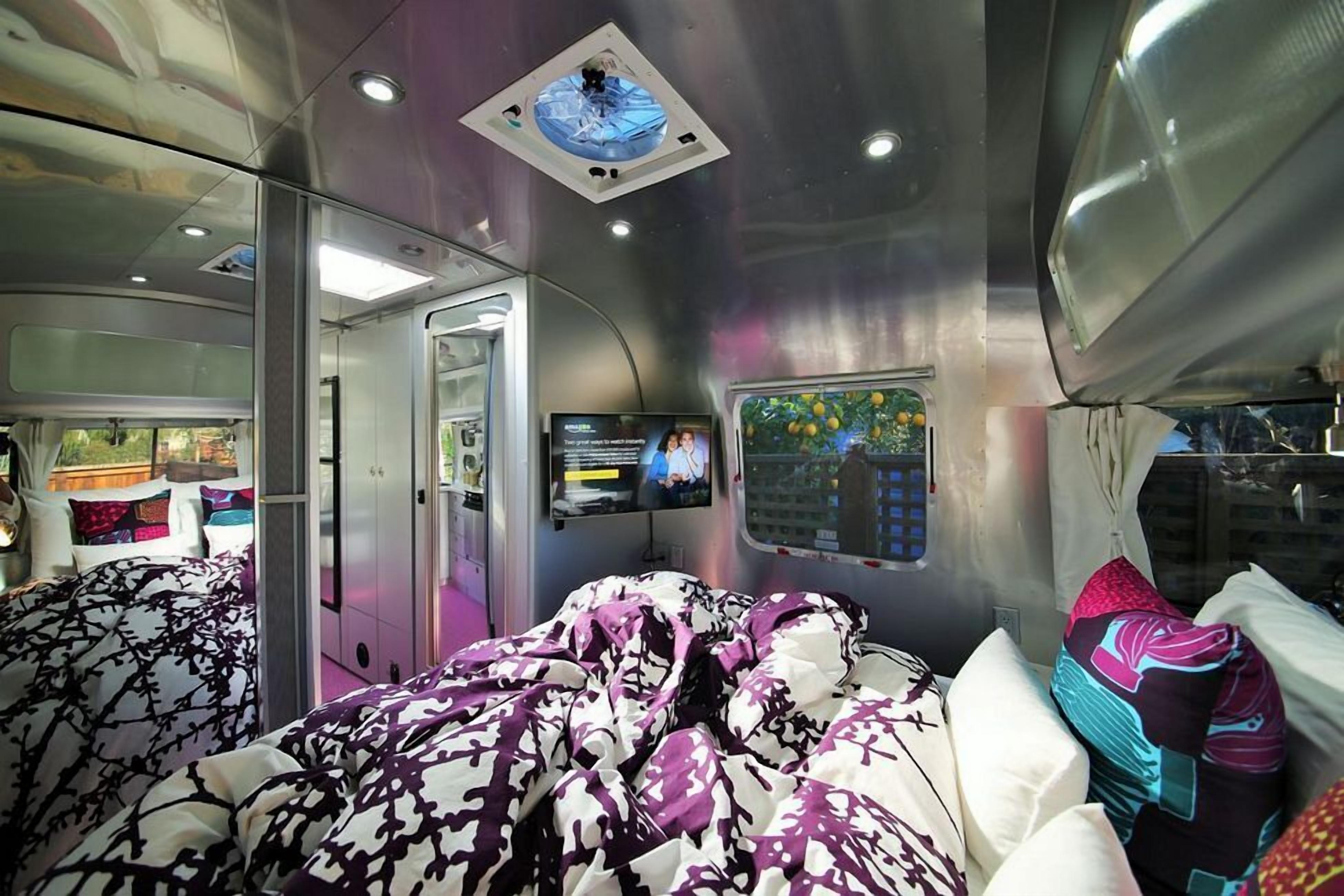 Un vagón de tren moderno con cama, televisión y ventana con vistas a follaje.