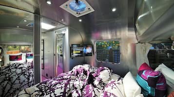 Un vagón de tren moderno con cama, televisión y ventana con vistas a follaje.