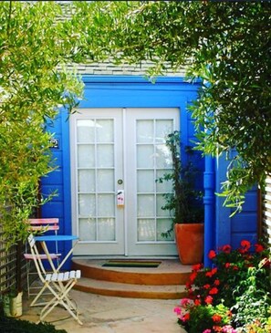 A blue building with a white door, a small outdoor seating area with a table and chairs, and a potted plant. - Metro Hotel and Cafe (Petaluma)