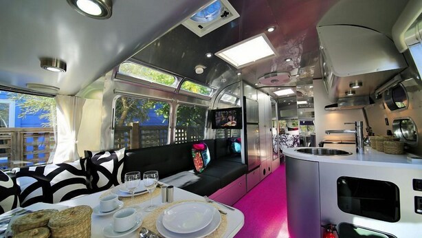 A dining area with a table set for two, a kitchen area with stainless steel appliances, and a seating area with a black and white patterned sofa. - Metro Hotel and Cafe (Petaluma)