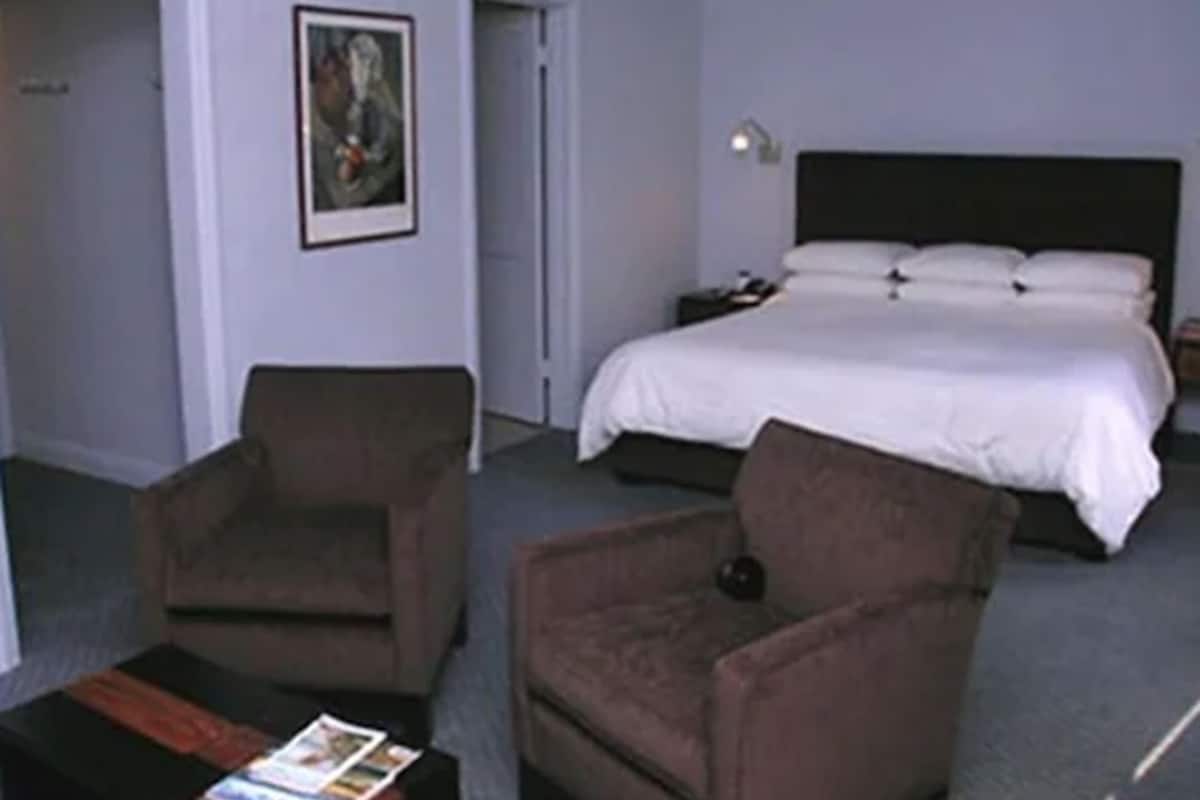 A hotel room with a bed, two armchairs, a nightstand, and a painting on the wall.