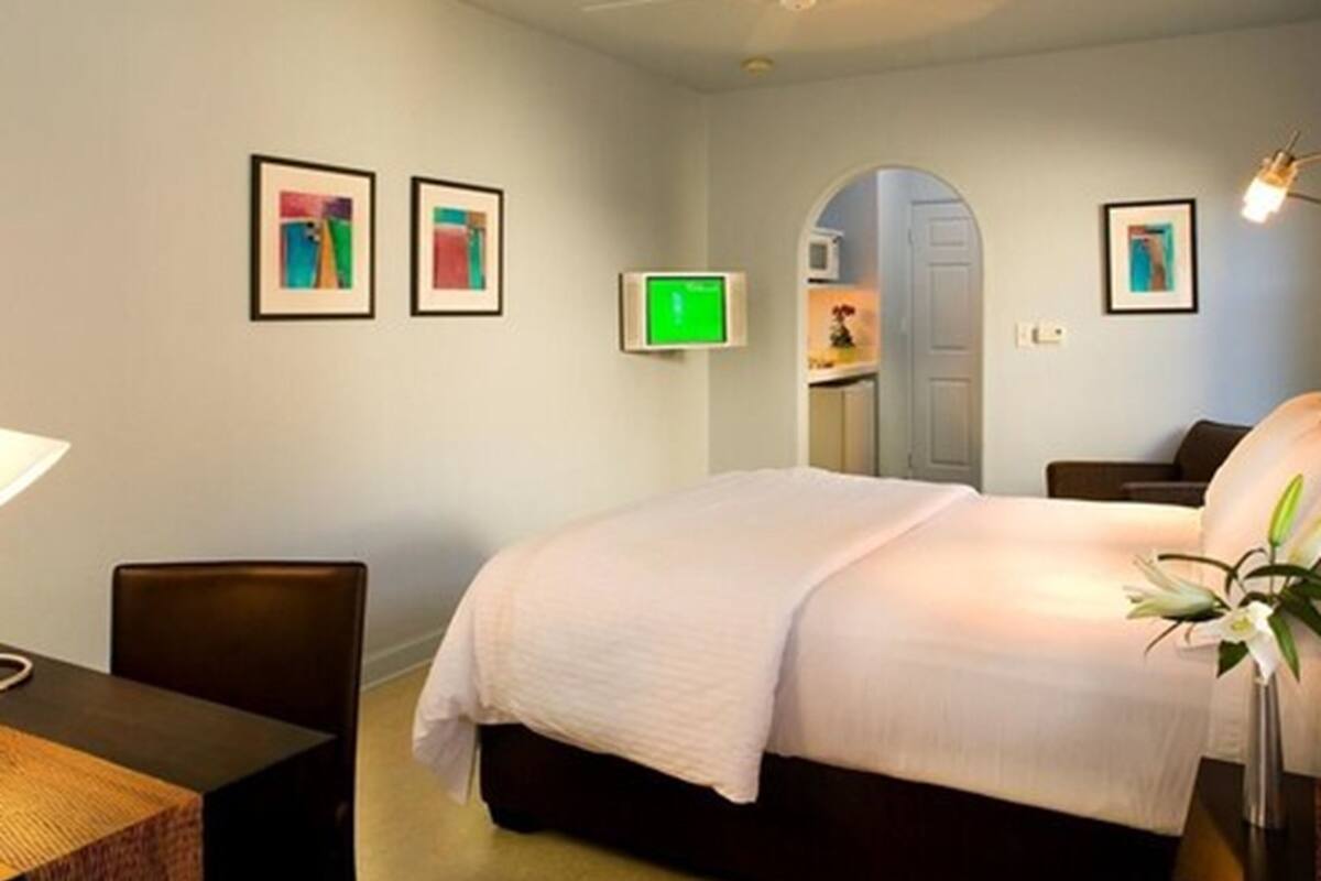 A hotel room with a bed, a desk, and a chair. There are framed pictures on the wall and a TV mounted on the wall.