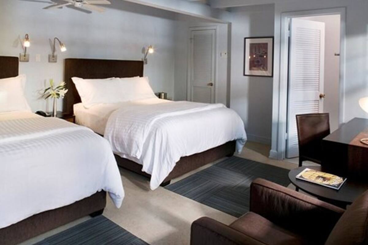 A hotel room with two beds, a ceiling fan, a desk with a chair, and a door.