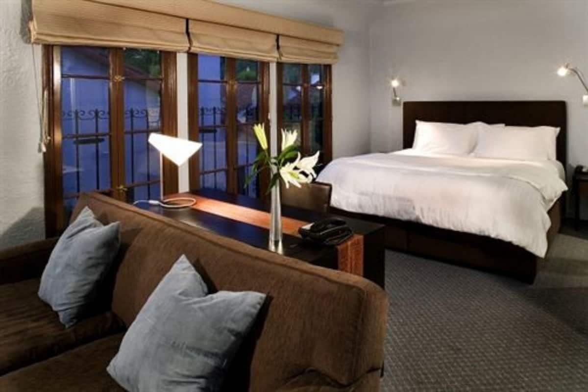 A hotel room with a bed, a sofa, a nightstand, a lamp, and a window with a view.