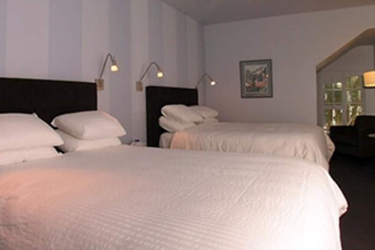 A hotel room with two beds, a ceiling fan, and a painting on the wall.