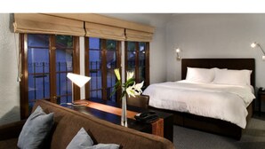 A hotel room with a bed, a sofa, a desk, and a window with a view of a balcony. - Casa Del Mar Inn (Santa Barbara)