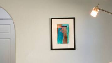 A framed abstract painting on a plain wall, a white door, and a floor lamp with a light bulb.
