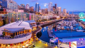 A waterfront hotel with a circular building, a marina with boats, and a Ferris wheel in the background. - Seattle Gaslight Inn (Seattle)
