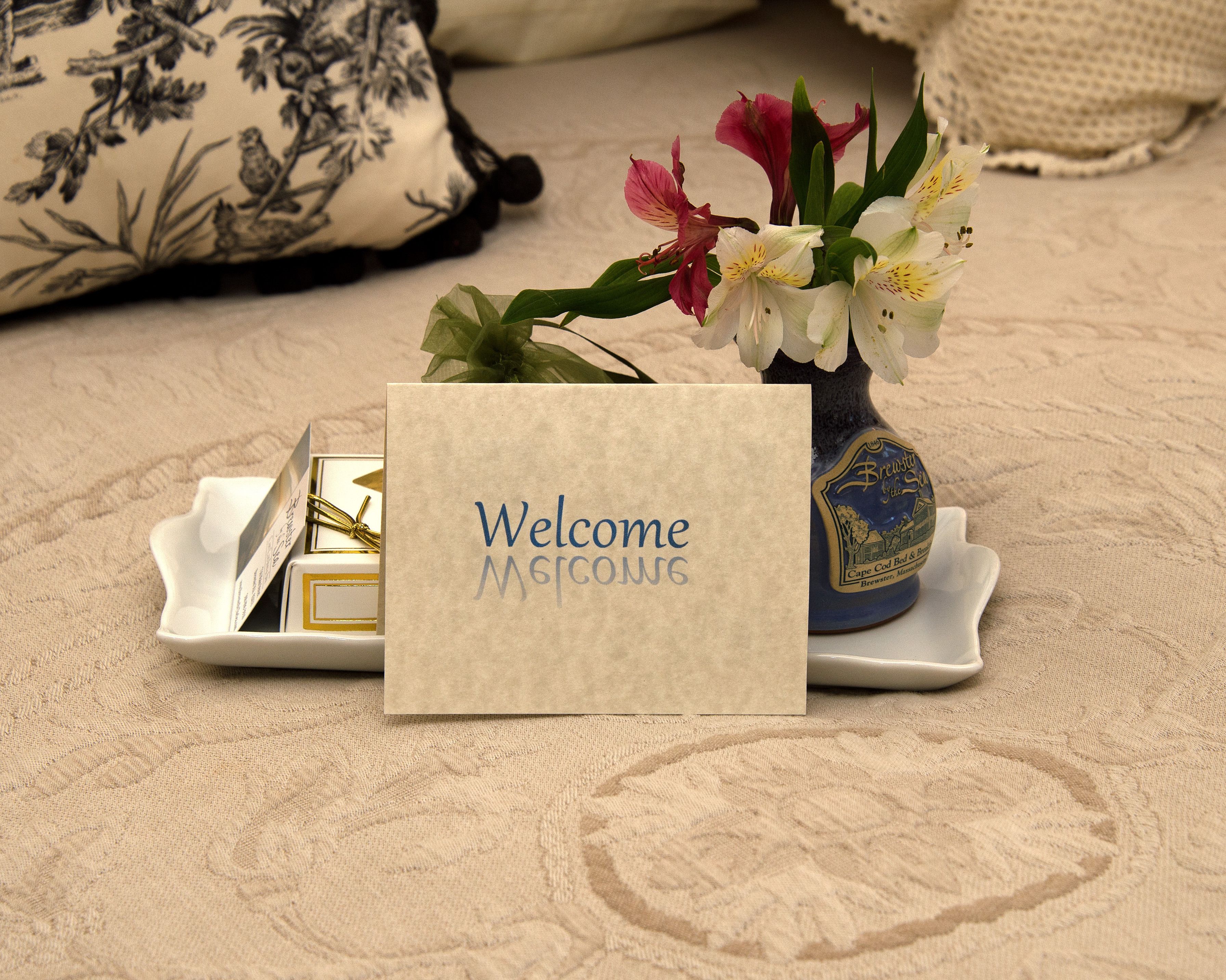 A welcome card, a vase with flowers, and a decorative plate on a textured surface.