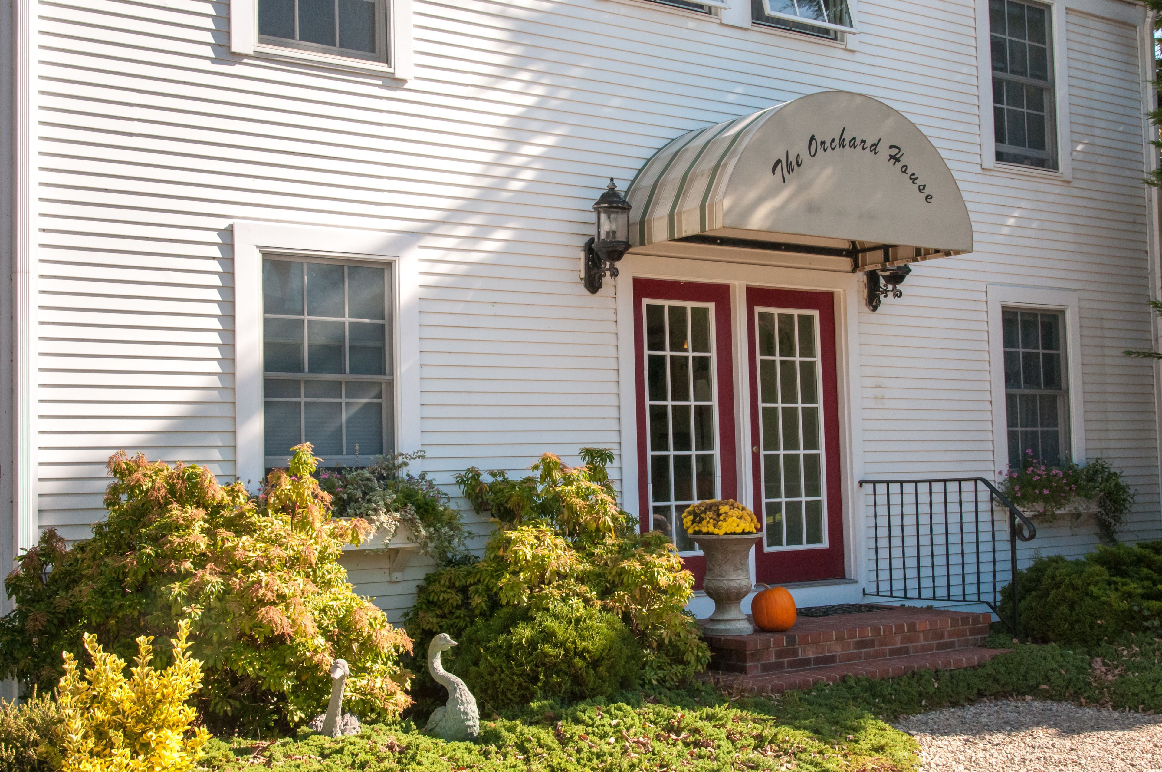 A white building with a red door and a sign that reads "The Orchard House."