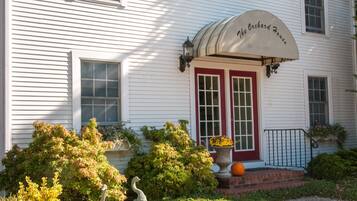 A white building with a red door and a sign that reads "The Orchard House."