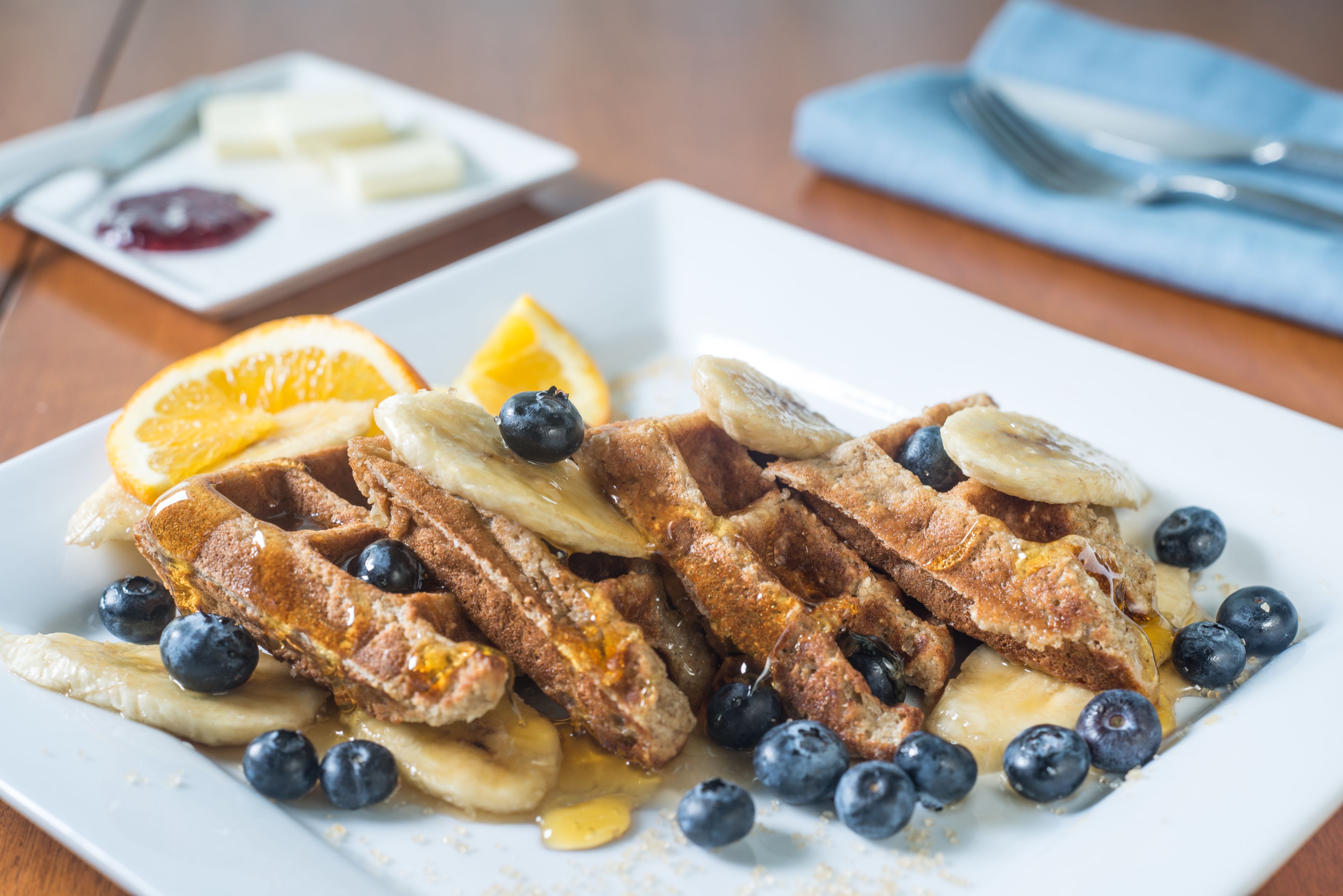 A plate of waffles with blueberries and orange slices, accompanied by a small dish of butter and jam.