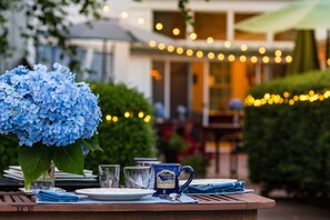 A table set with plates, glasses, a mug, and a blue hydrangea. - Brewster by the Sea Inn (Brewster)