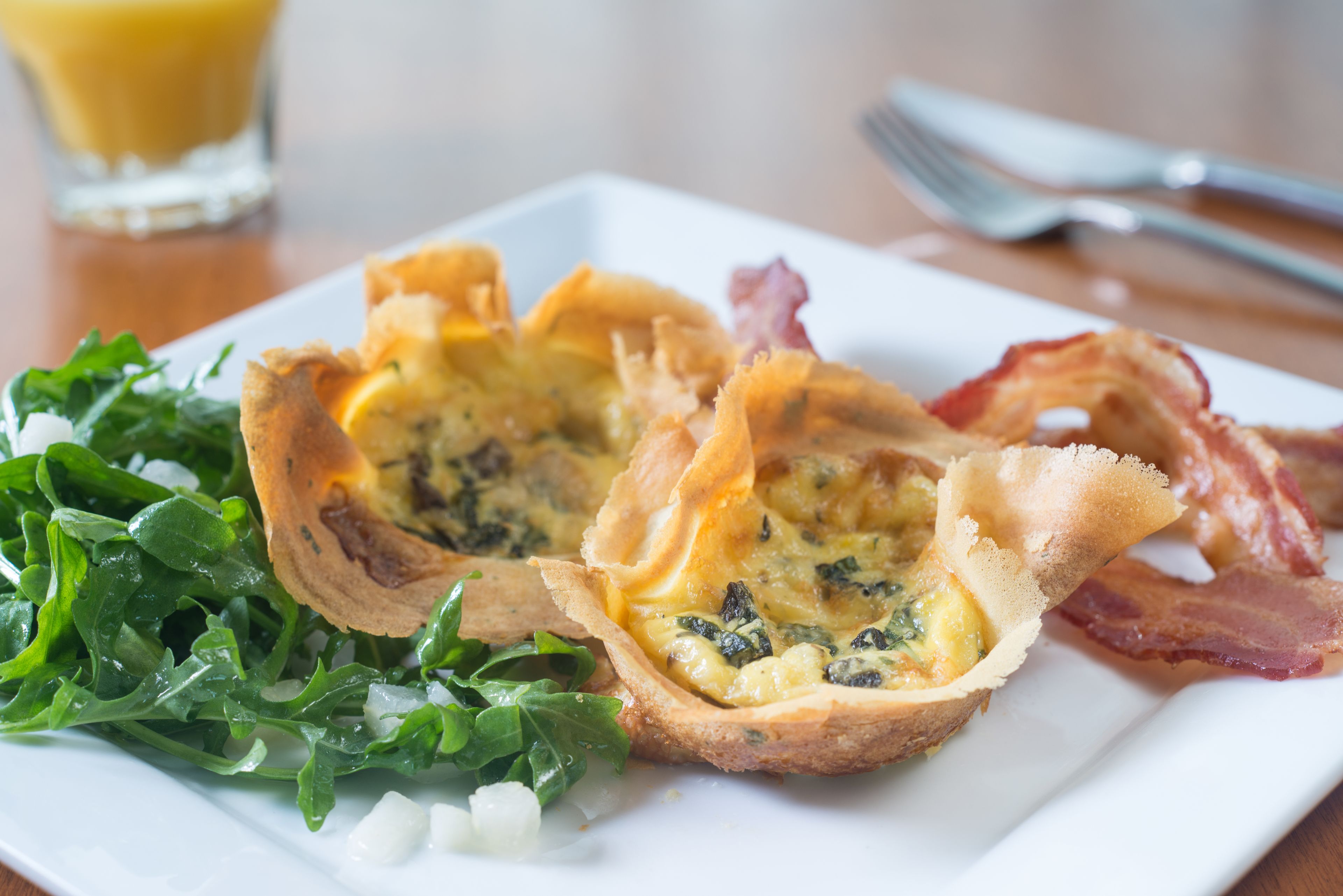 A breakfast plate with a quiche, bacon, and greens.