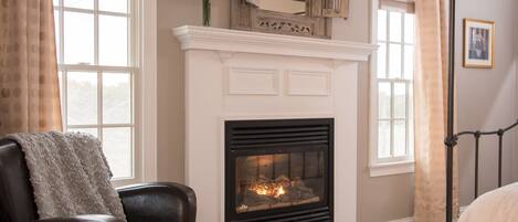 A living room with a fireplace, a large window, and a black leather chair.