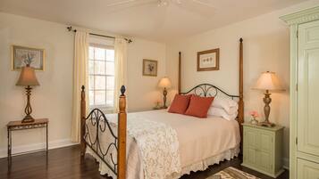 A bedroom with a four-poster bed, a nightstand with a lamp, a dresser, and a window with curtains.