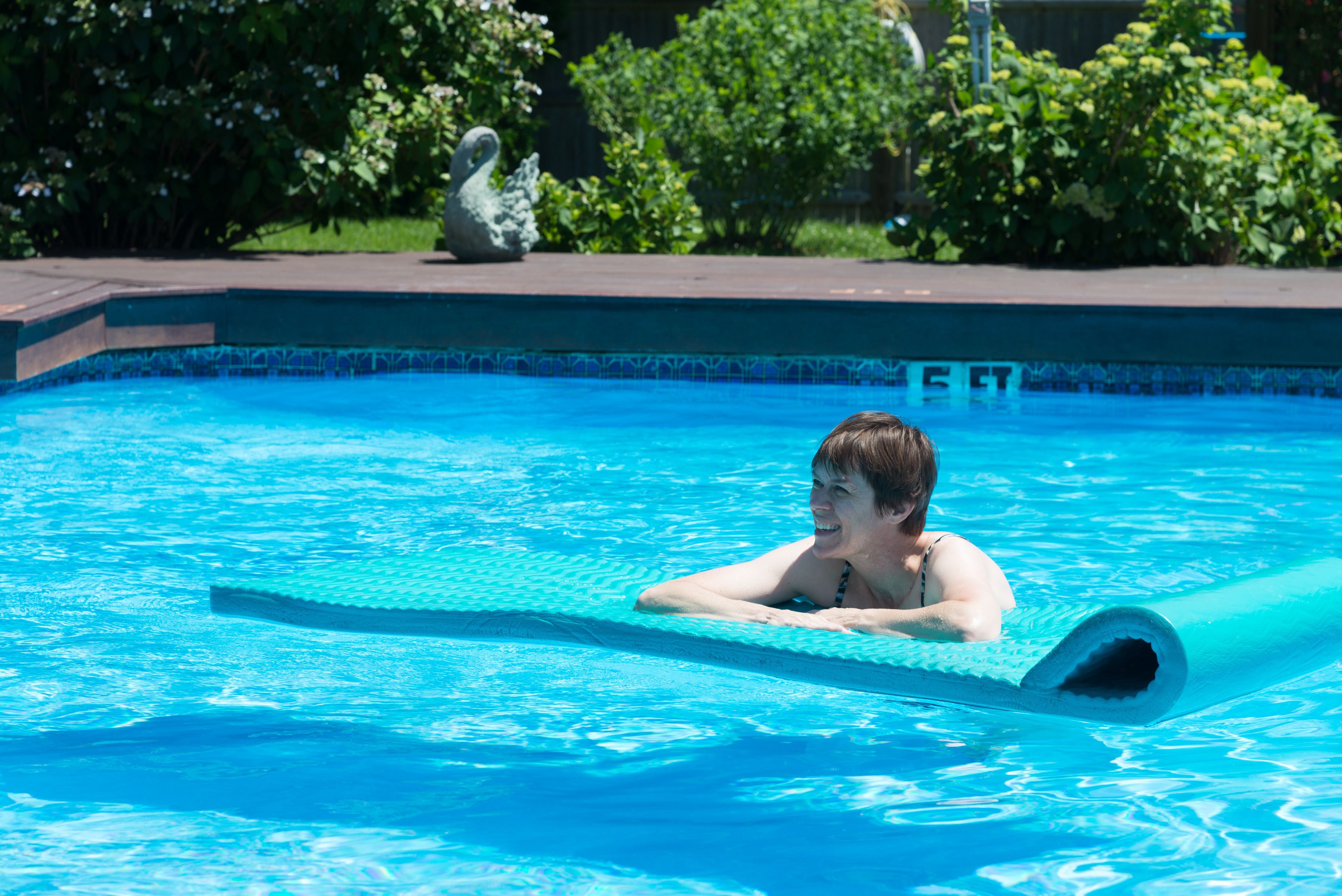 A person in a swimming pool with a clear blue water edge and a swan statue in the background.