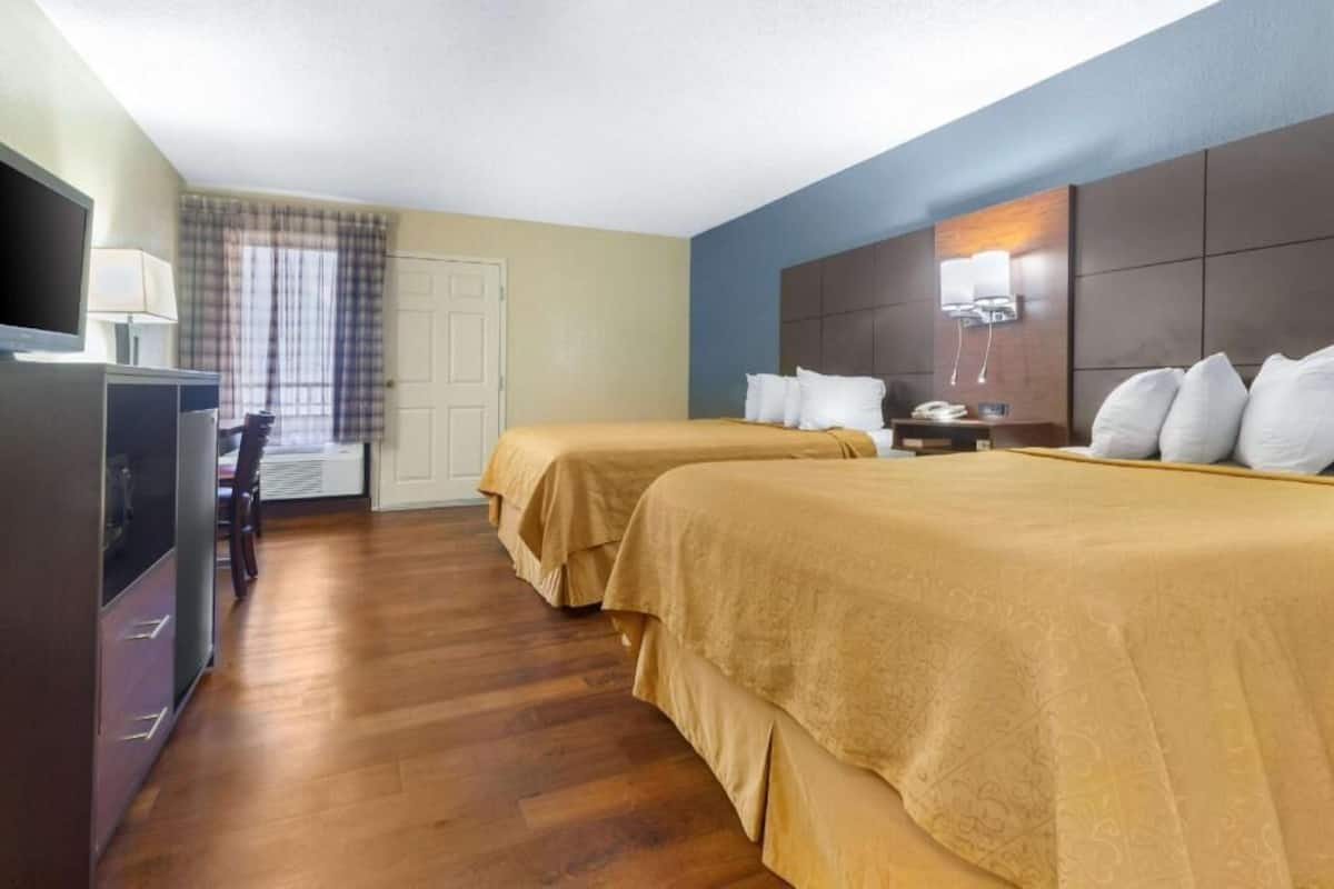 A hotel room with two beds, a TV, a desk, and a chair.