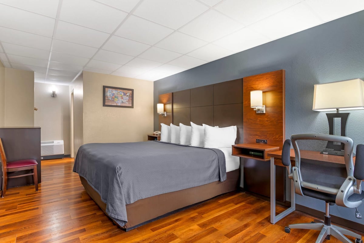 A hotel room with a large bed, a desk with a chair, a desk lamp, and a wall-mounted lamp.
