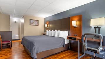 A hotel room with a large bed, a desk with a chair, a desk lamp, and a wall-mounted lamp.