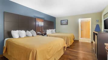 Een hotelkamer met twee bedden, een bureau, een televisie en een deur naar een andere kamer.