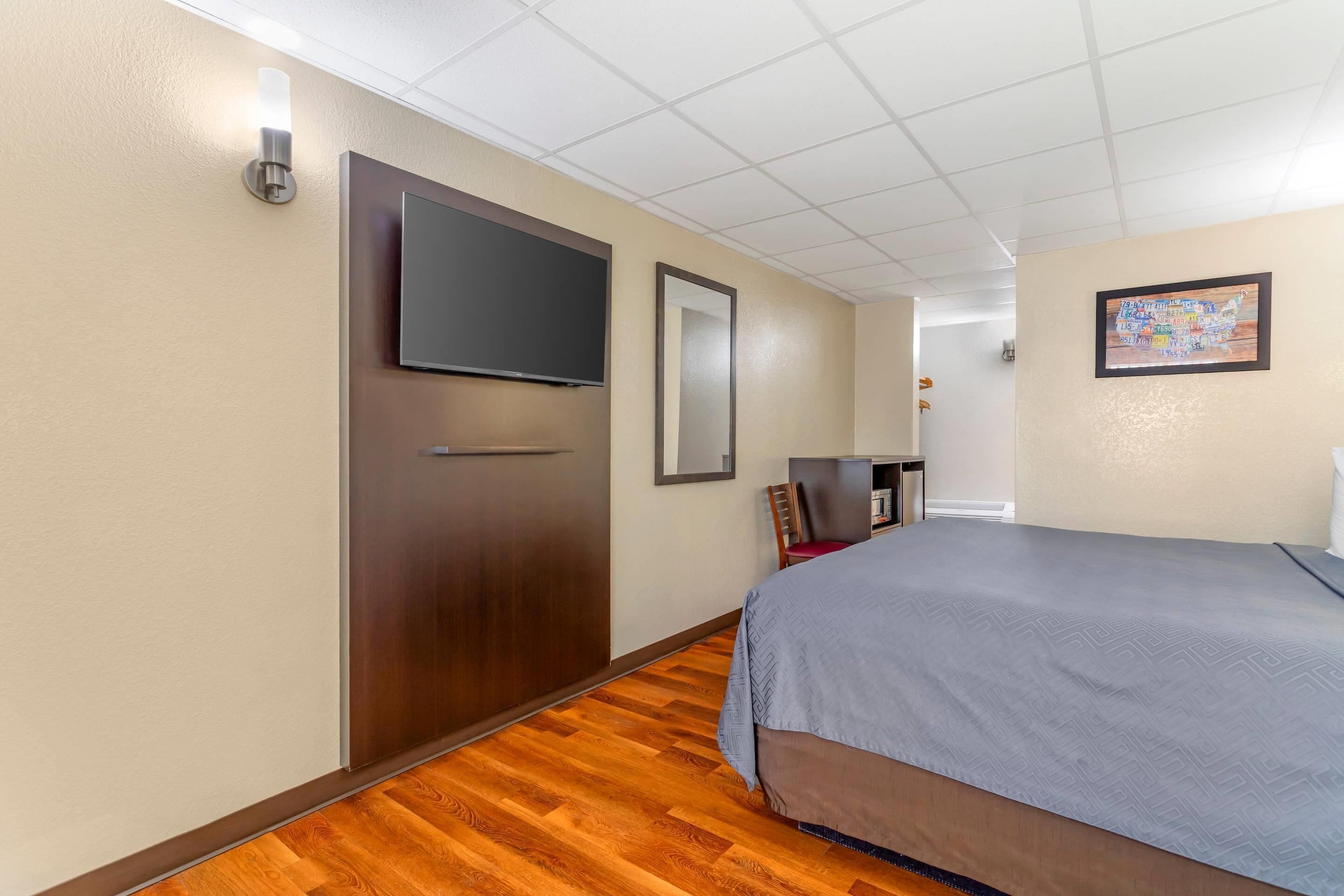 Una habitación de hotel con una cama grande, un televisor de pantalla plana montado en la pared, suelo de madera y un mapa enmarcado en la pared.