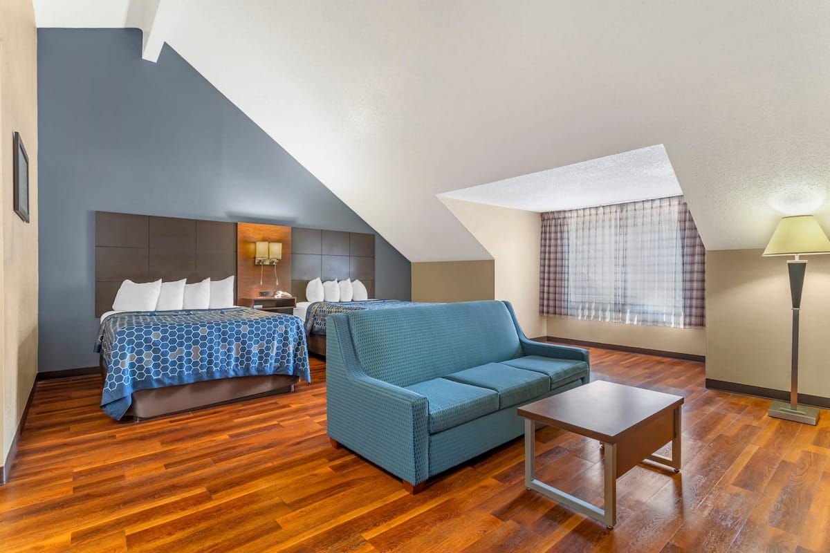 A room with a bed, a sofa, a small table, and a lamp.