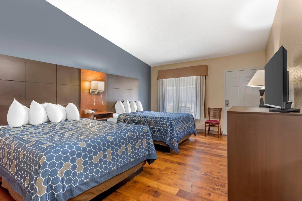 A hotel room with two beds, a desk, a chair, a television, and a window with curtains.