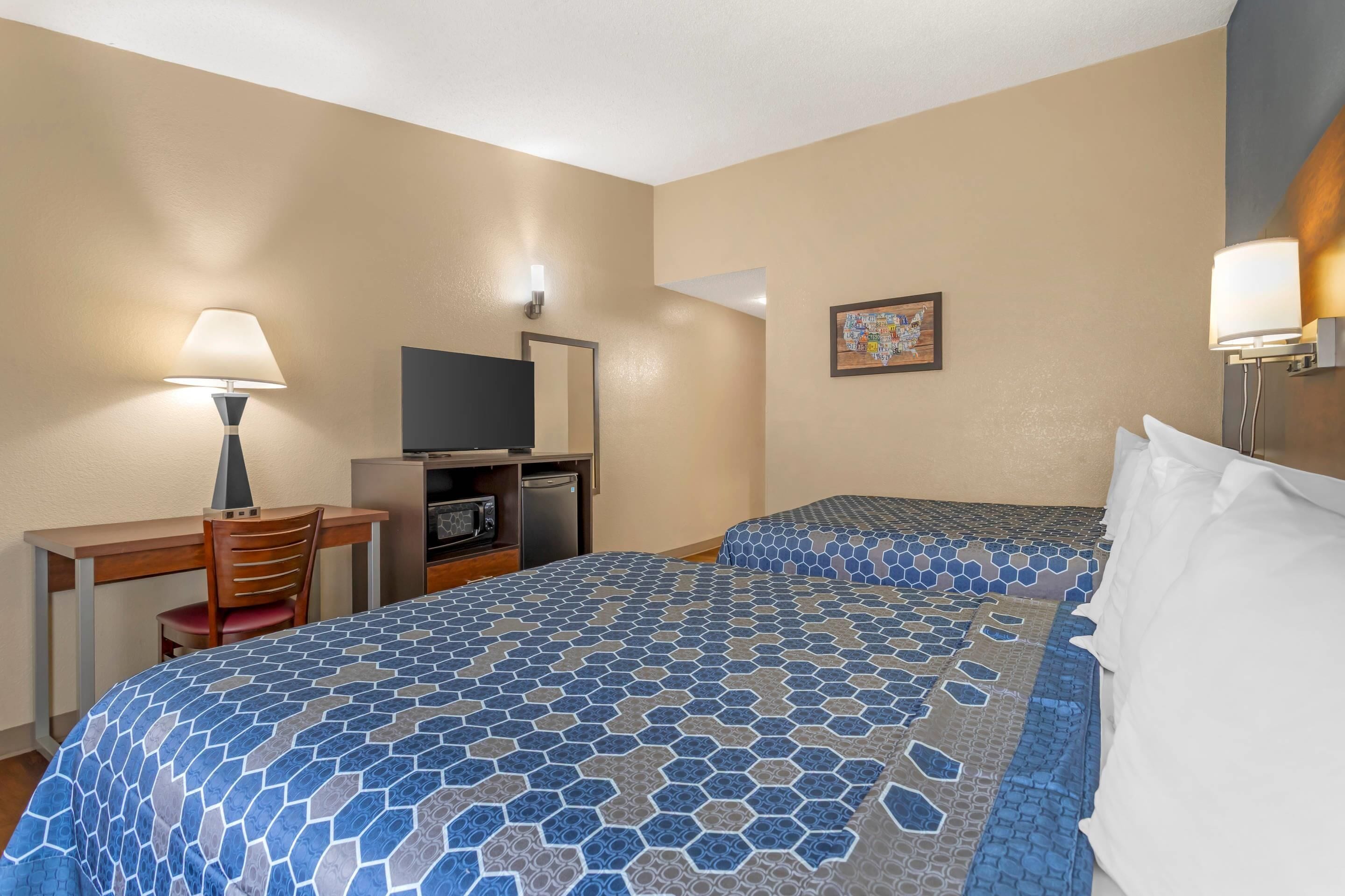 Habitación de hotel con dos camas, un escritorio con silla, televisión y una kitchenette pequeña.