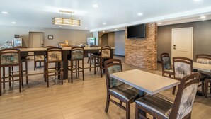 A modern dining area with multiple tables and chairs, a stone accent wall, and a flat-screen TV mounted above the seating area. - Elevate Hotel at Sierra Blanca (Ruidoso)