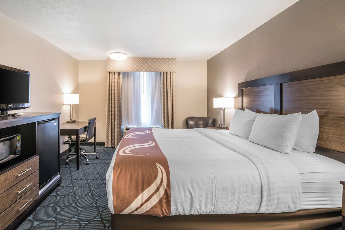 A hotel room with a large bed, a desk with a chair, a television, and a minibar.