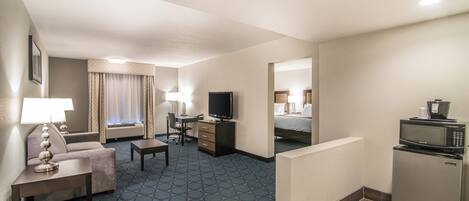 A hotel room with a sofa, a desk, a television, a bed, and a refrigerator.