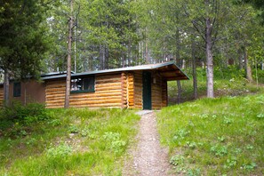 A log cabin with a dirt path leading to it, surrounded by trees. - Colter Bay Village (Moran)