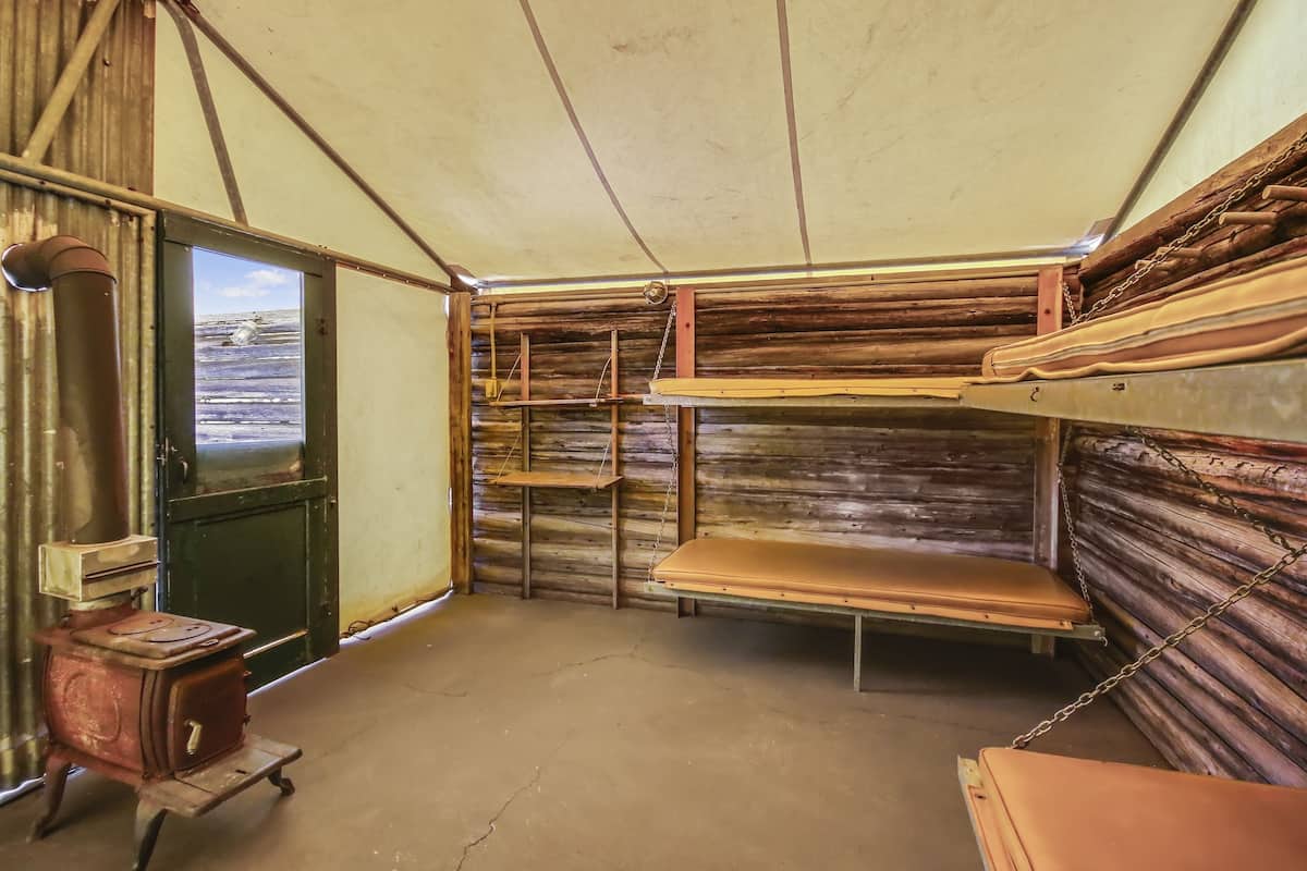 A rustic interior with wooden walls, a metal stove, and shelves with wooden planks.