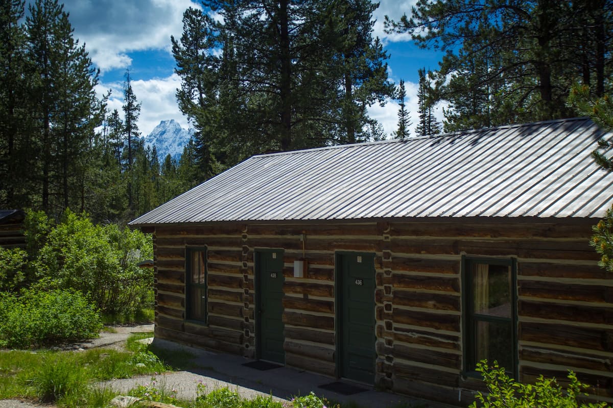A log cabin with a metal roof, two green doors, and a window.