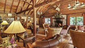 A log cabin interior with leather furniture, a stone fireplace, and a deer head mounted on the wall.